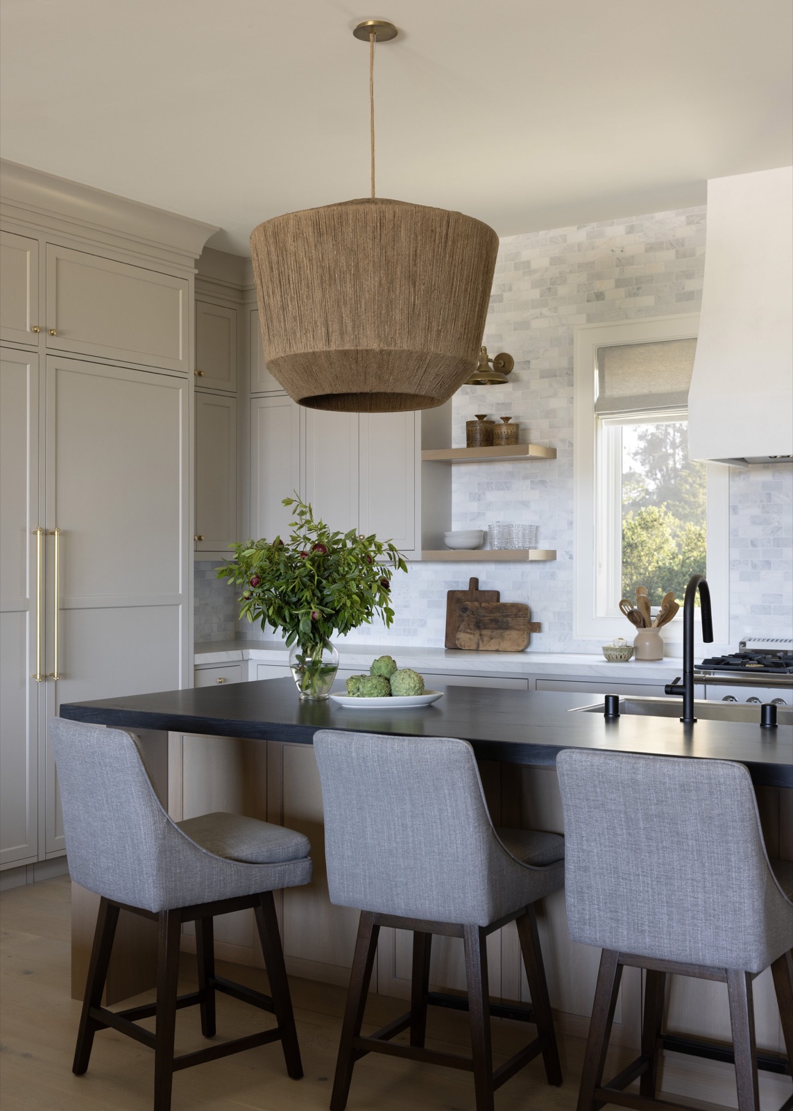 Kitchen with a woven pendant and dark stone island.