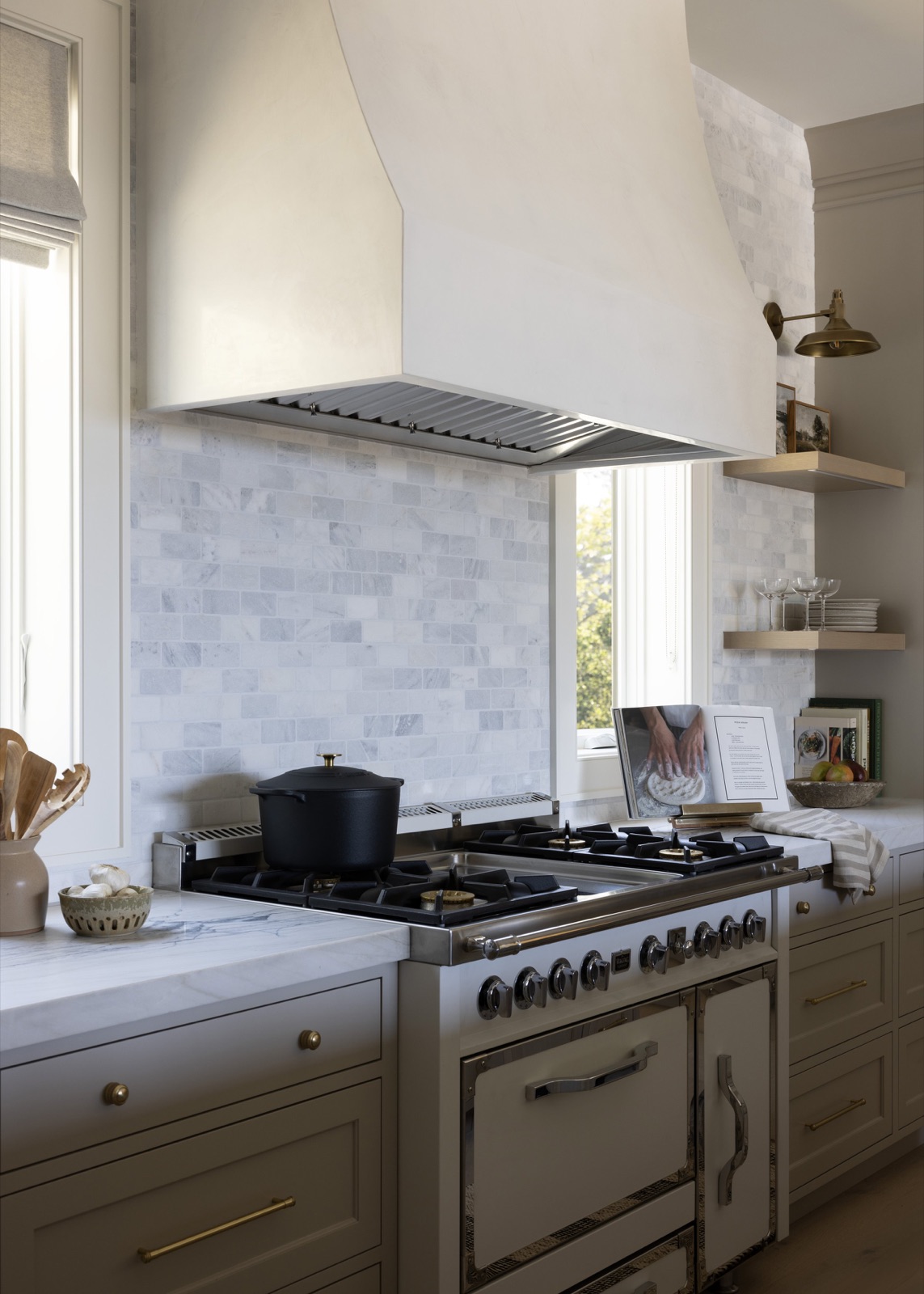 A professional range beneath a plaster hood and marble backsplash.