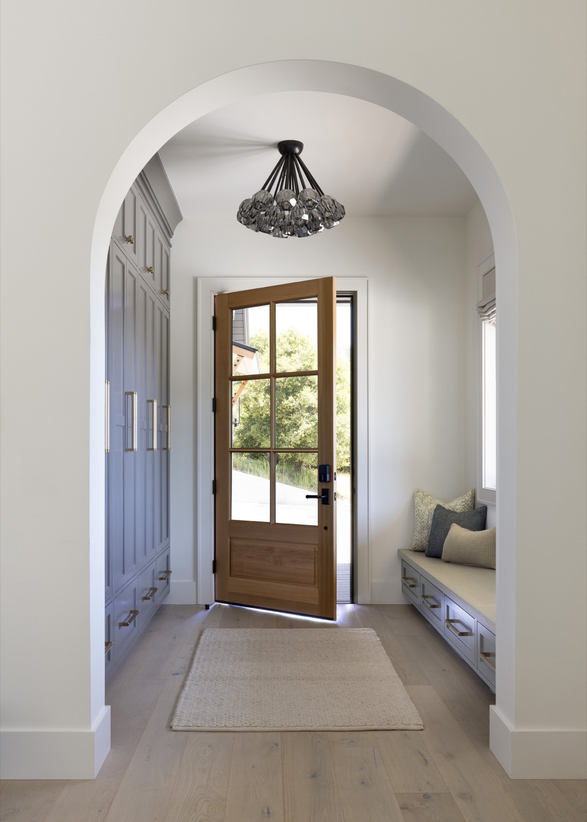 The entry hall through an arched opening, a glass-paneled wood front door beneath a smoked crystal chandelier.