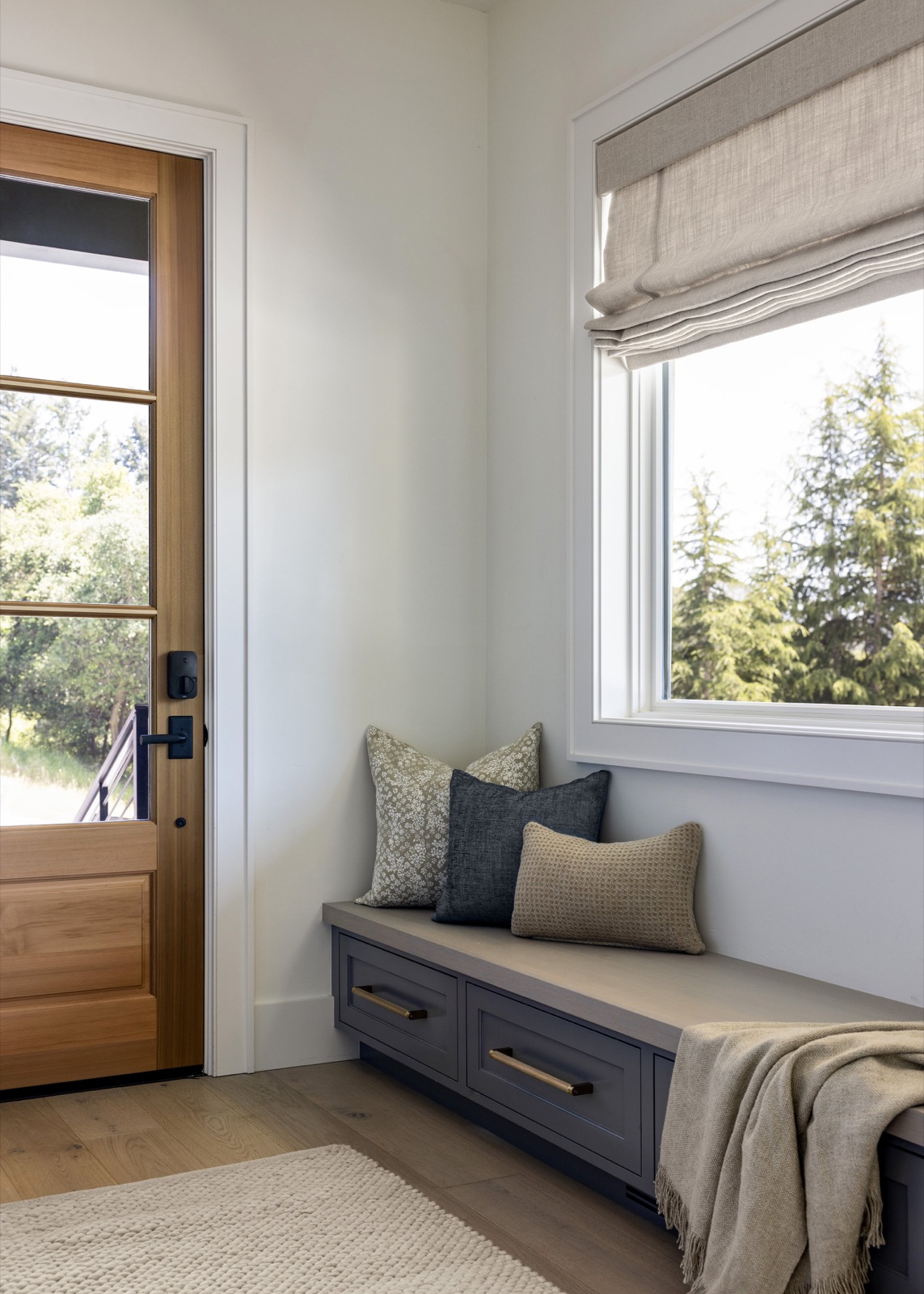 The mudroom bench by the front door, layered pillows and a linen roman shade.