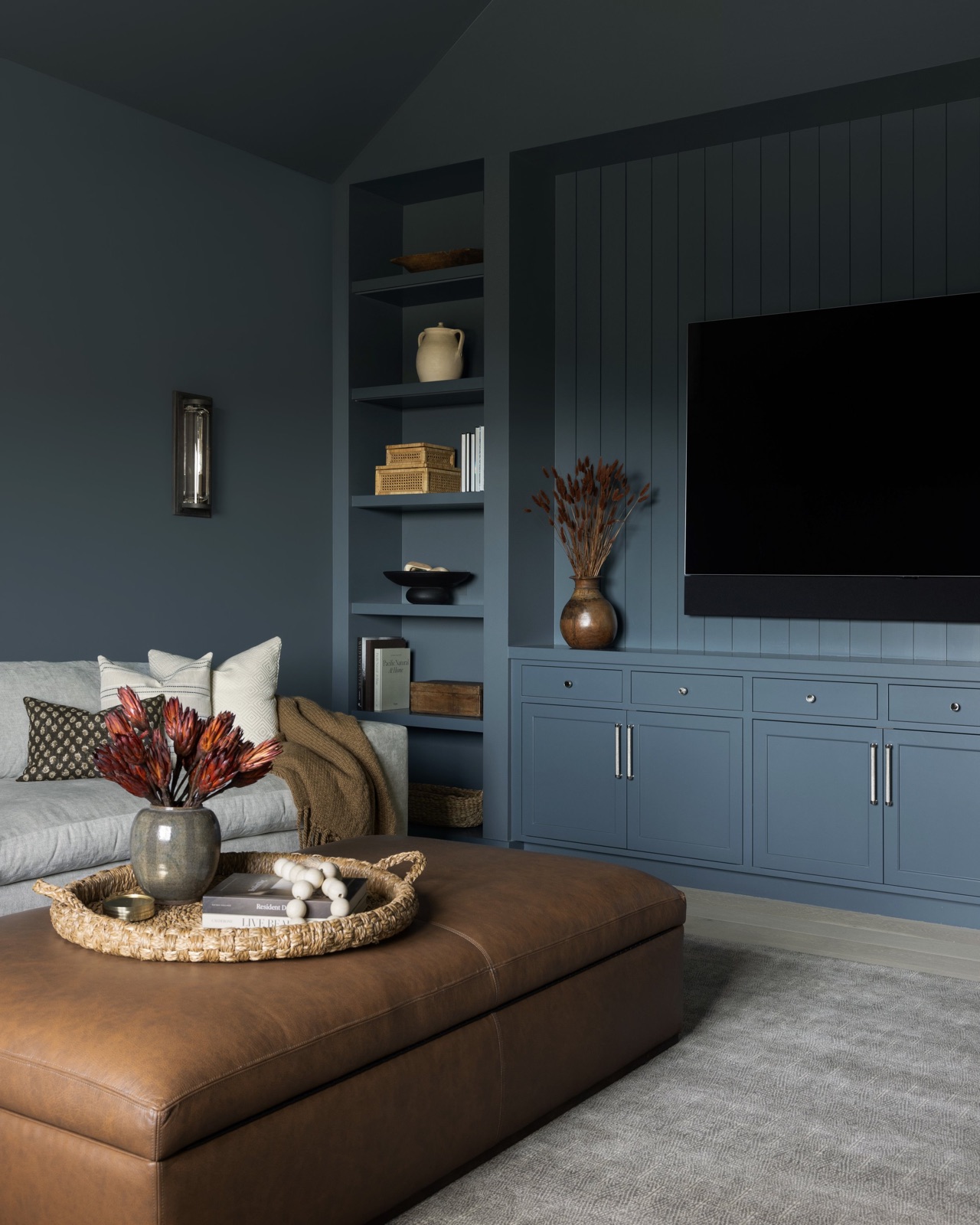 The media room, blue-gray built-ins and a tan leather ottoman.