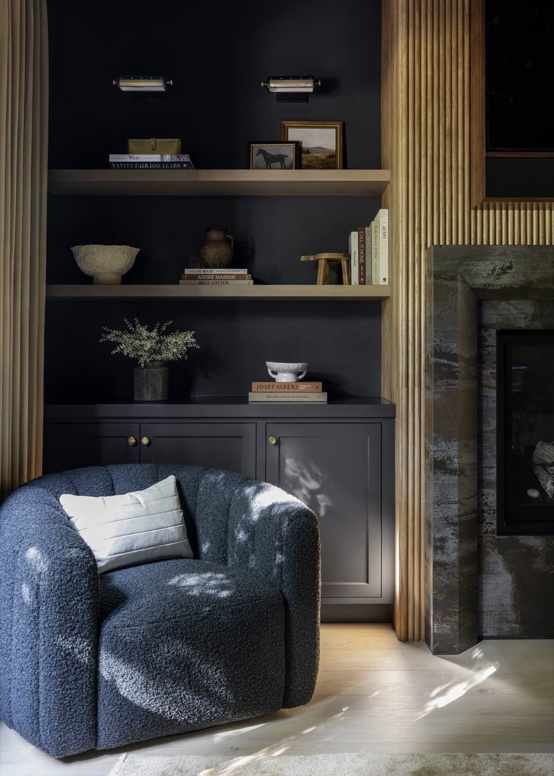 A paneled reading nook with floating wood shelves and a boucle armchair.