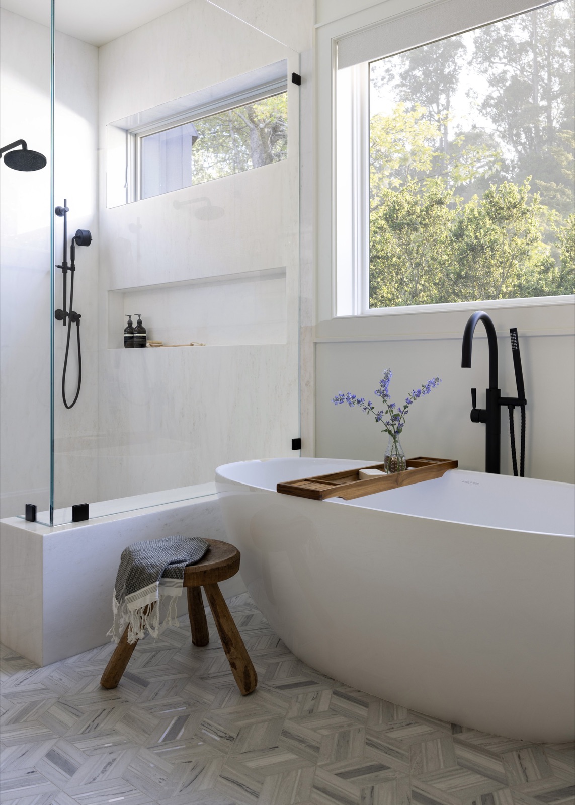 Primary bath, freestanding tub, black fixtures, and a window to the trees.