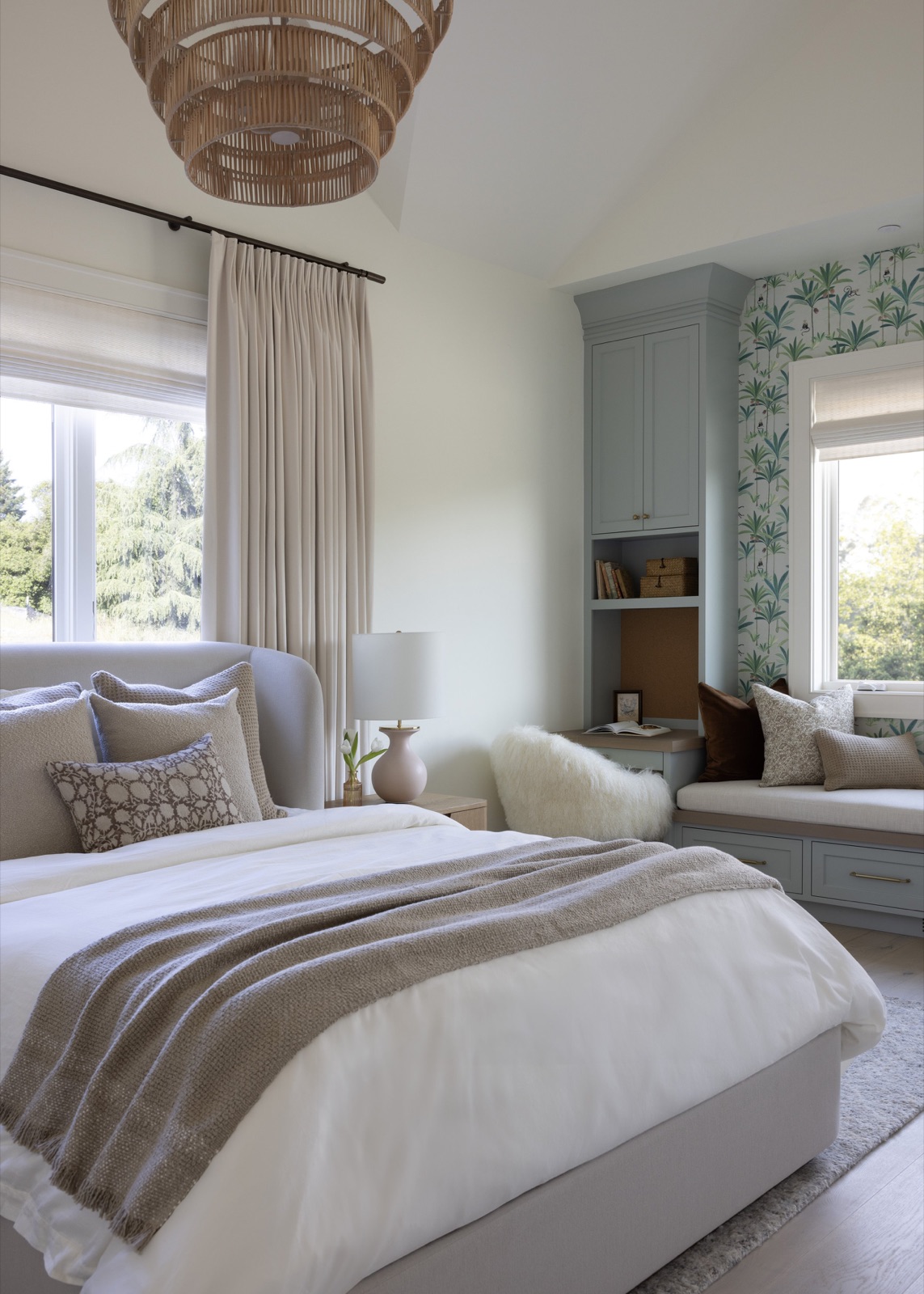 A guest bedroom, upholstered bed under a rattan pendant with a window seat beyond.