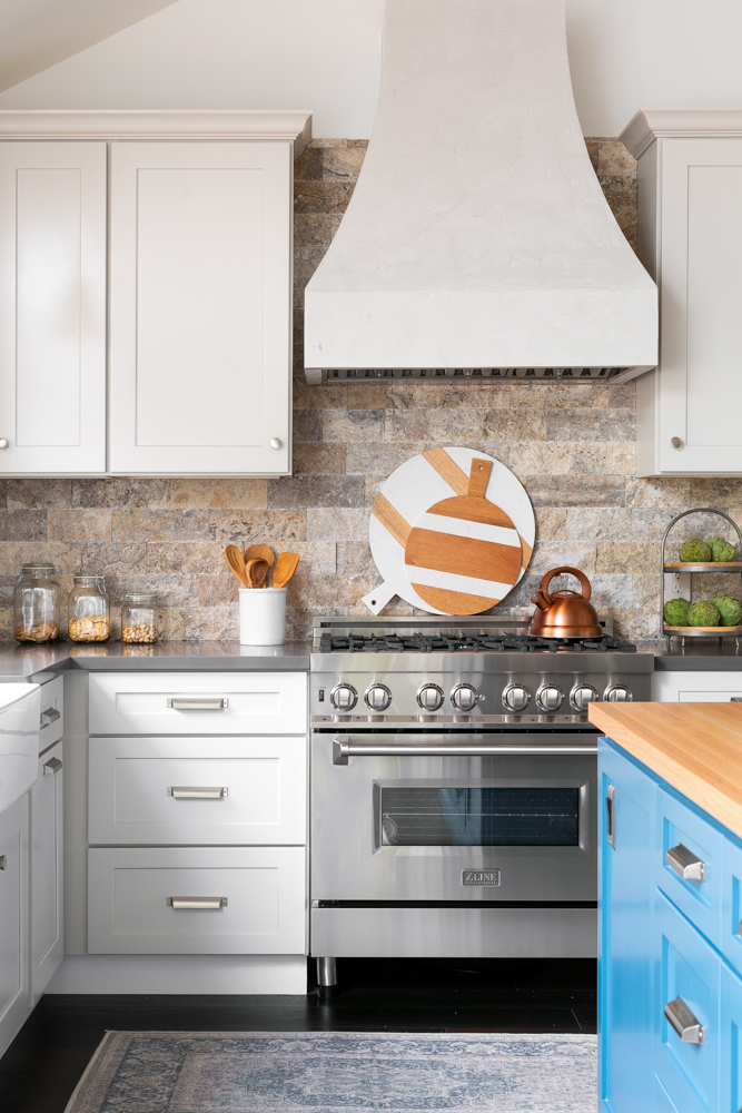 The kitchen, a plaster range hood over a natural stone backsplash and professional range.