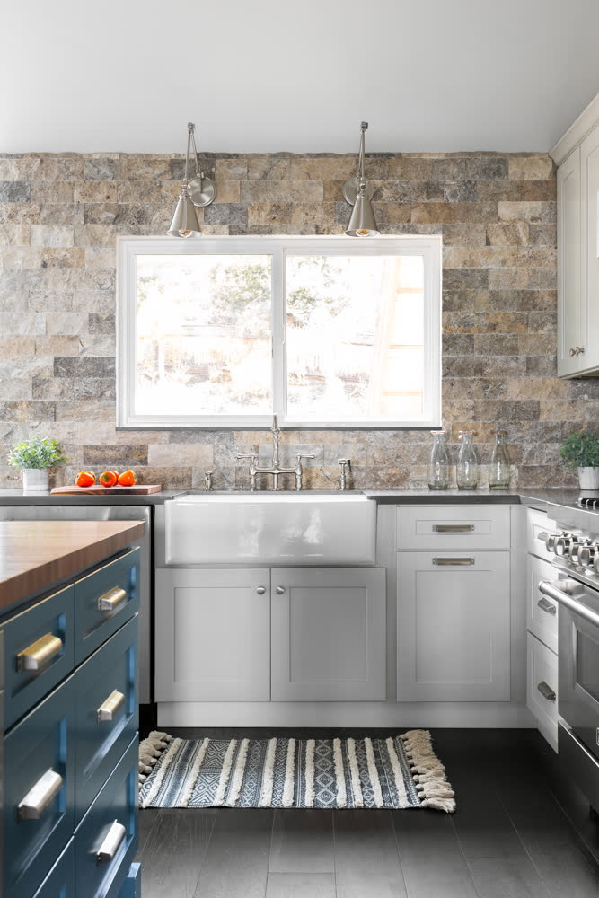 A farmhouse sink beneath nickel sconces and the stone accent wall.