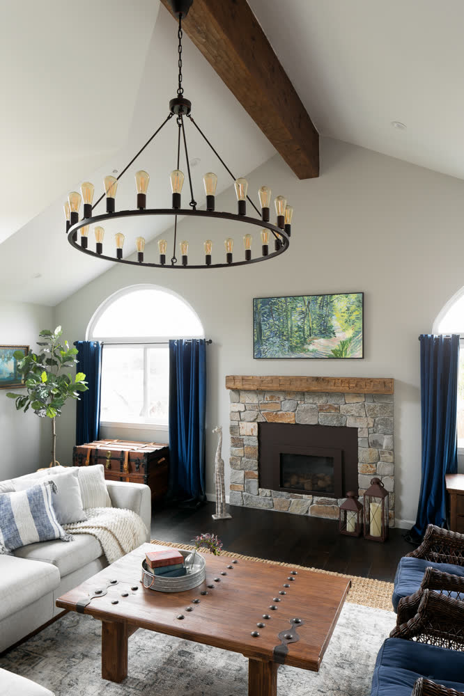 The living room, a vaulted ceiling with timber beam, wagon-wheel chandelier, and stone fireplace.